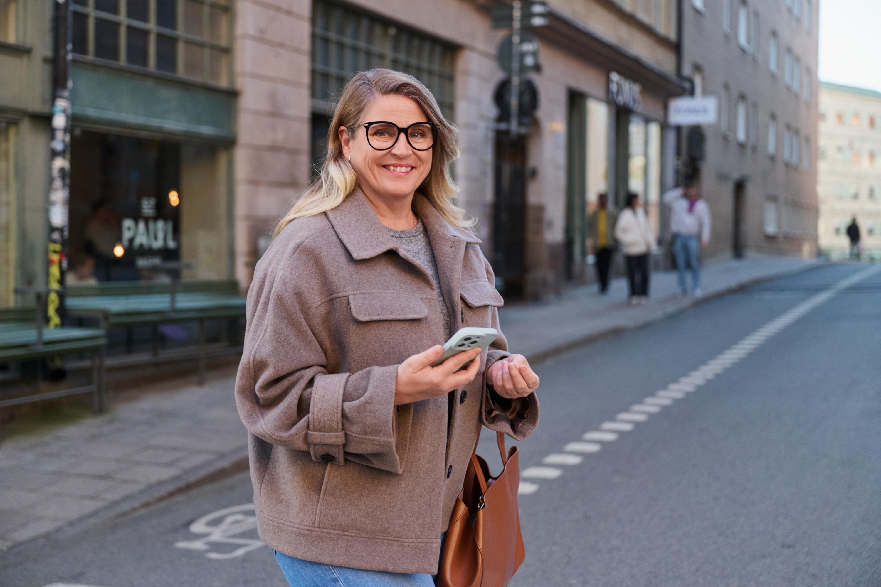 En kvinna går i en stad hållandes i en mobil