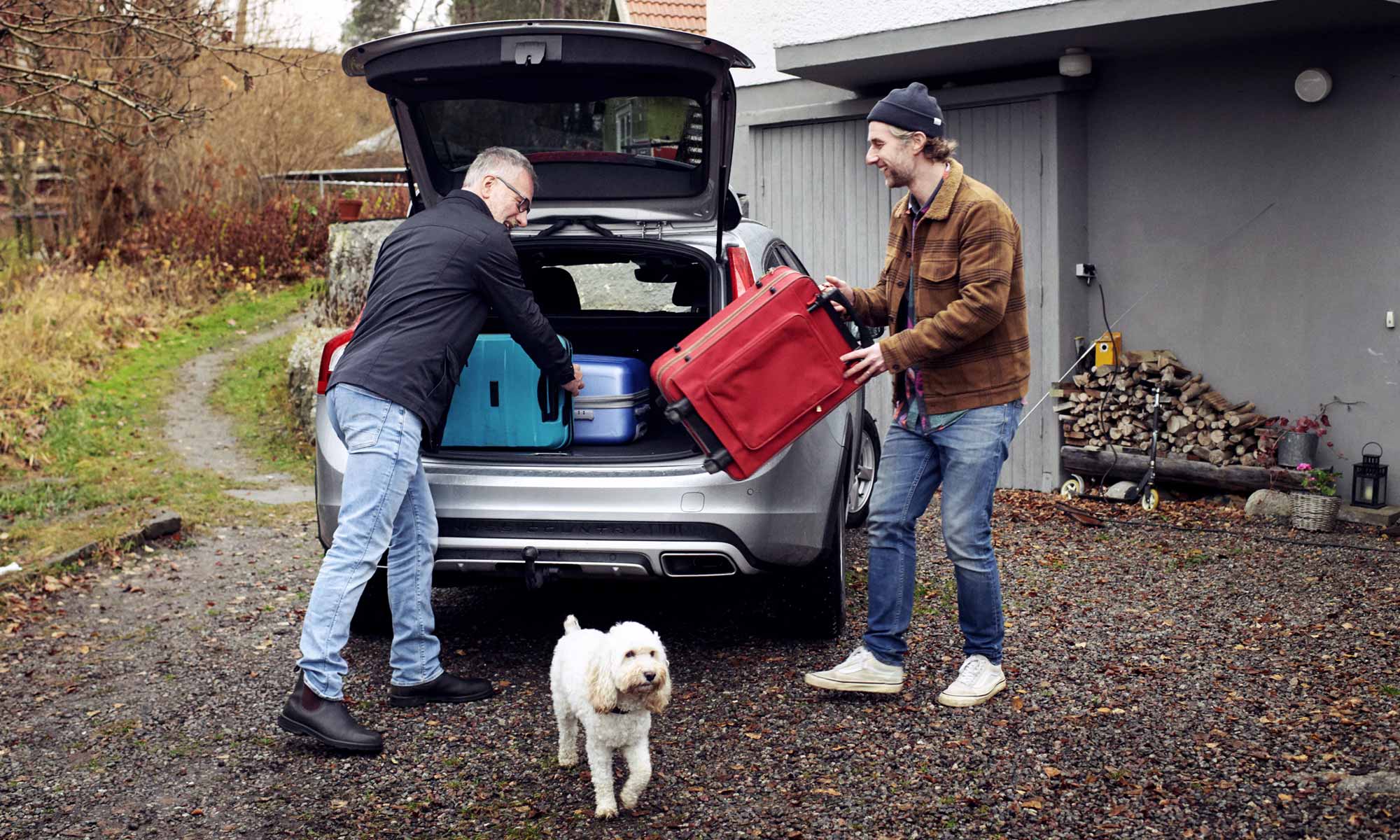 Två män packar in bagageväskor i en baklucka på en bil en ruggig höstdag
