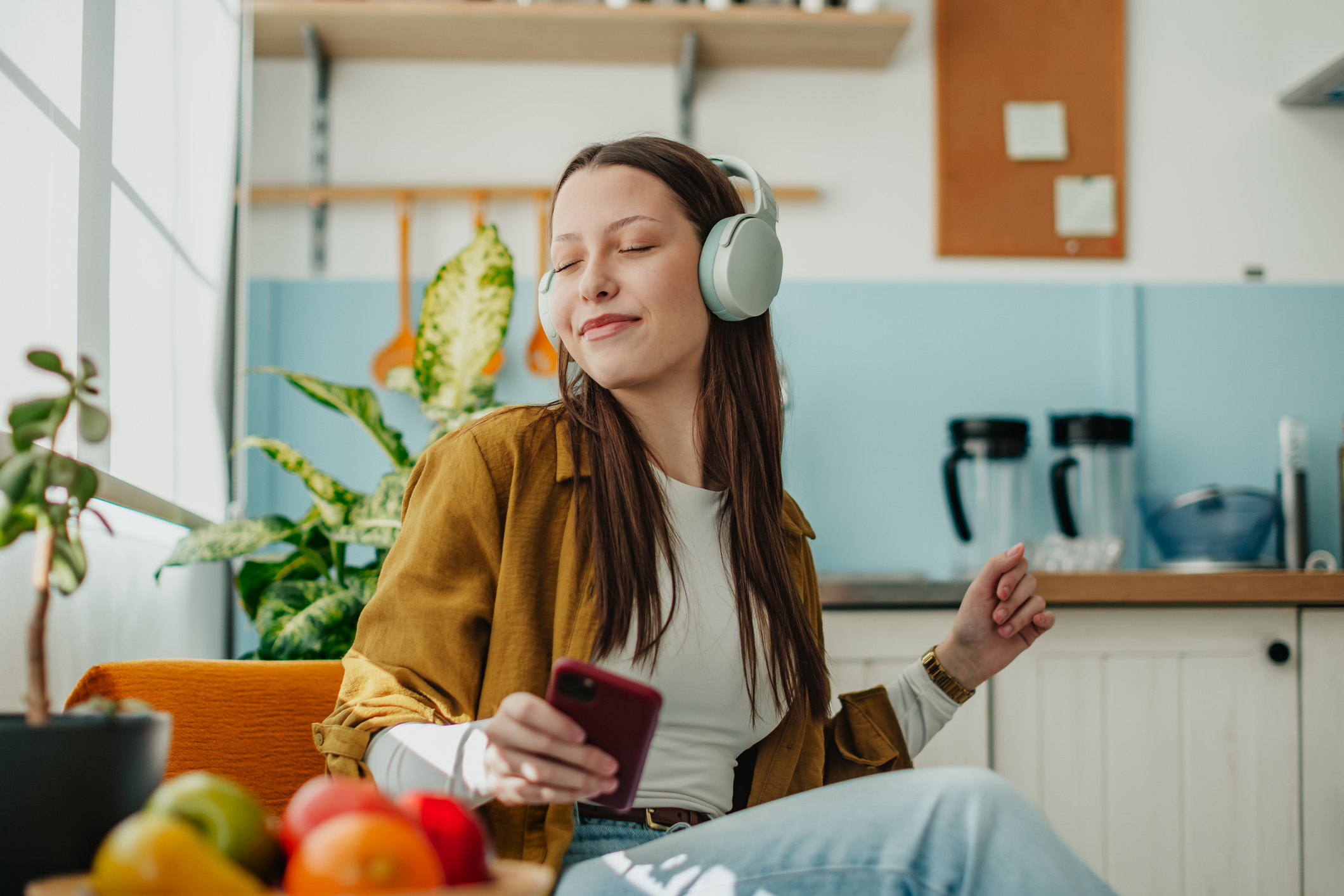 Ung kvinna sitter på en stol i köket med hörlurar och lyssnar på musik